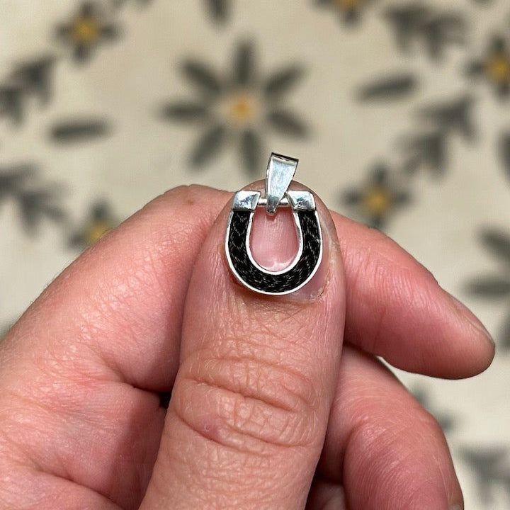 Hand holding a horseshoe pendant with horsehair inlay the size of a thumbnail. 