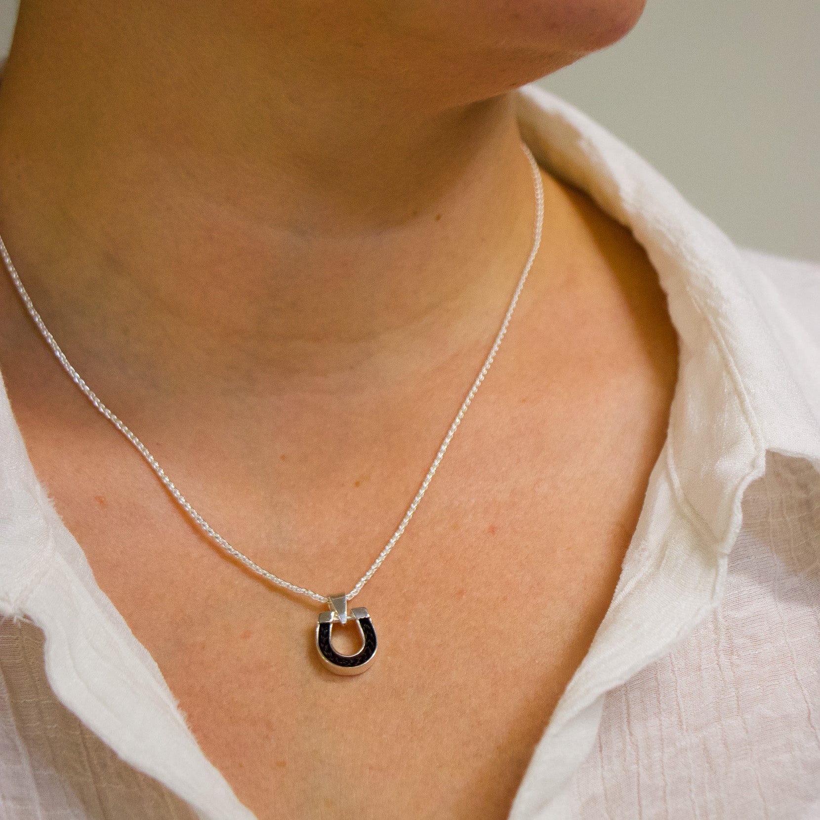 Person wearing a tiny horseshoe charm with horsehair inlay. 