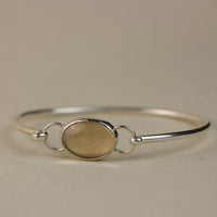 Silver bracelet with a dog fur oval charm on a beige background